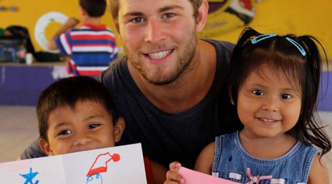 A Projects Abroad Youth Development volunteer with two children holding their drawings. Two children showing their art with a Projects Abroad volunteer on his Youth Development Project.